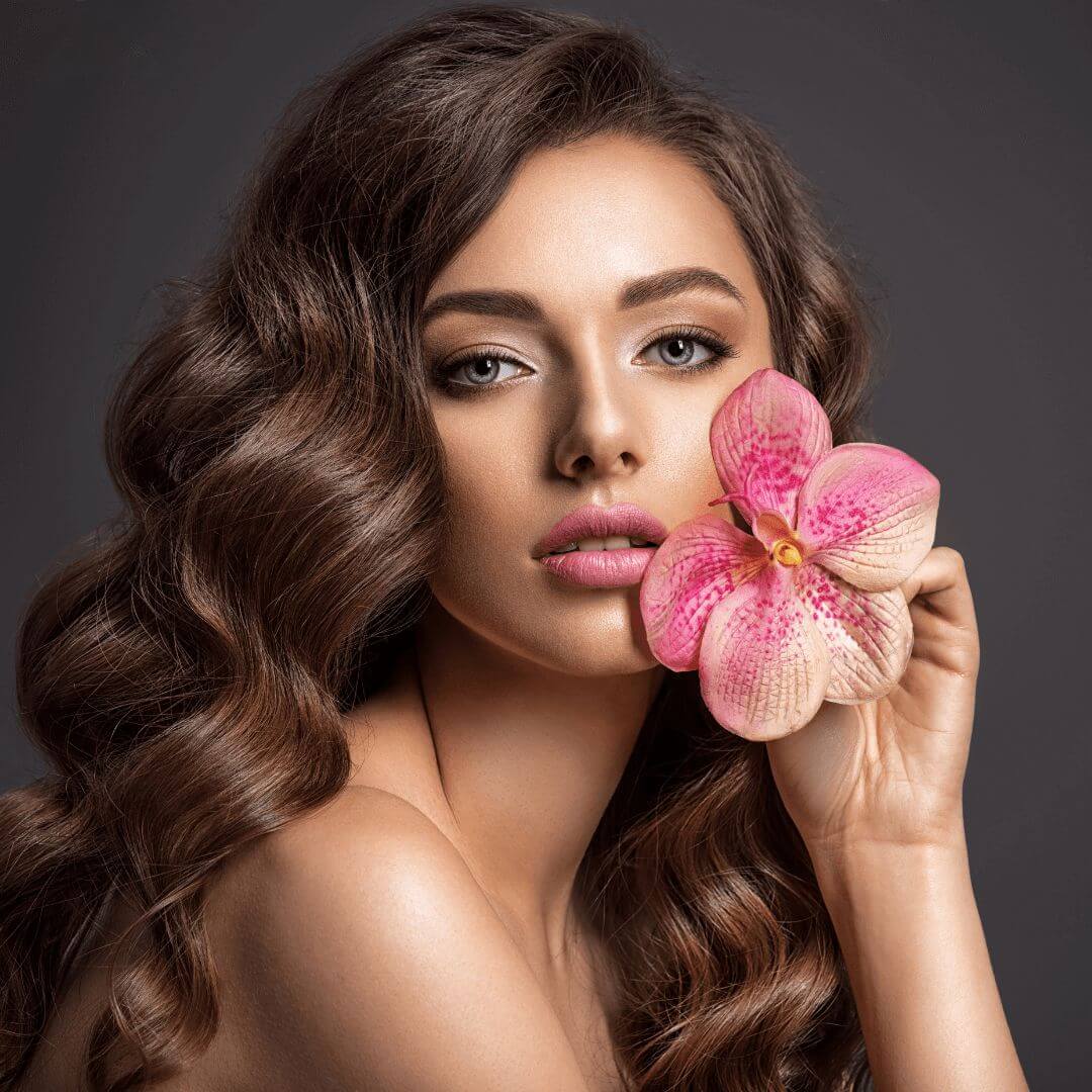 Girl with long brown, curly hair holding a flower.