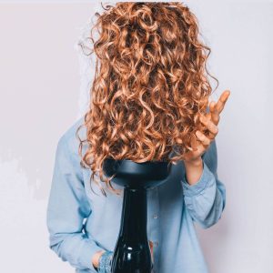 Young woman diffusing her curly hair. 