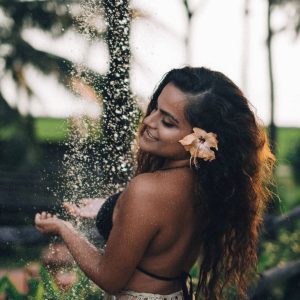 Girl with long curly hair, wearing a bikini, standing in an outdoor shower.