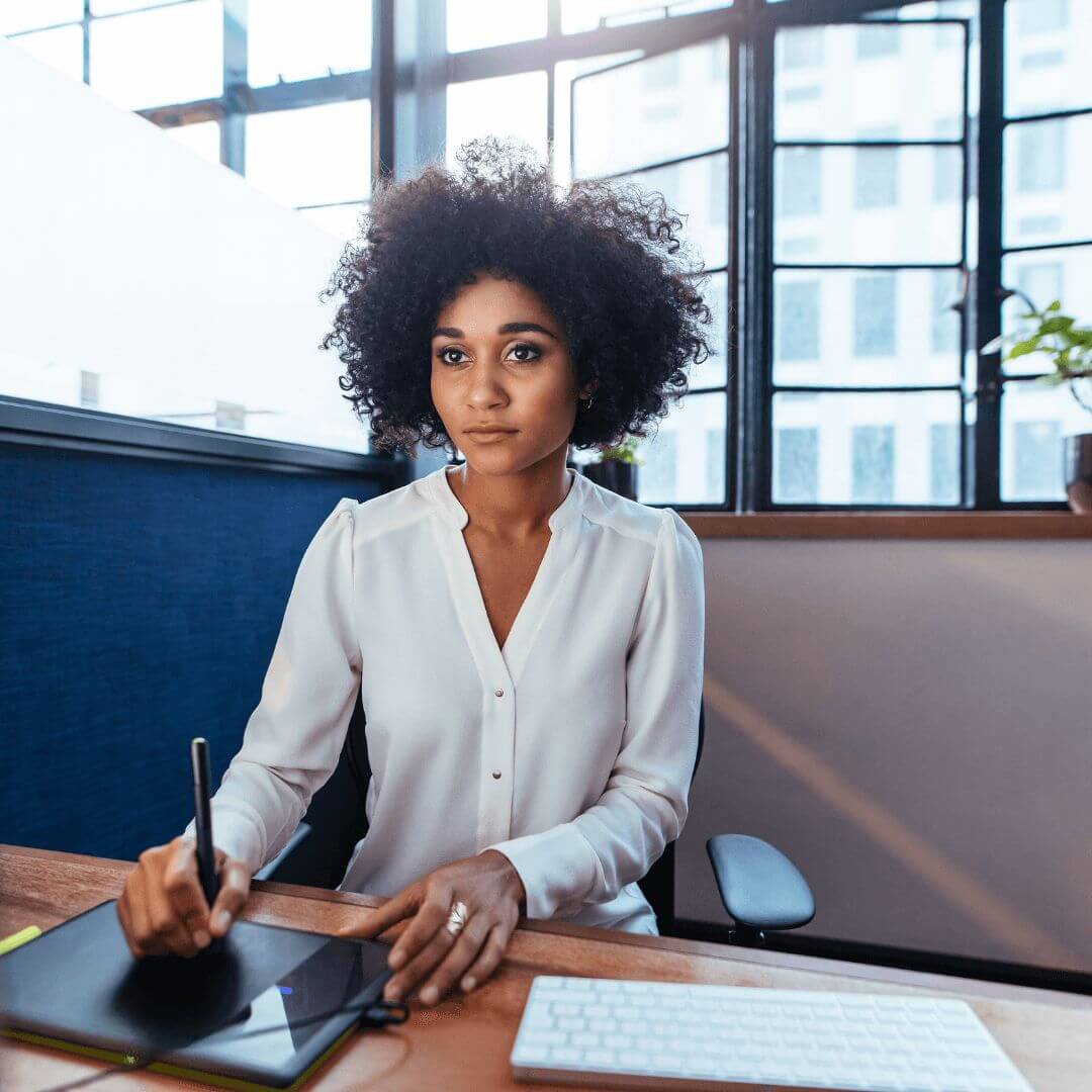 Young woman sitting at a desk, with chin length curly hair, wearing a white blouse.