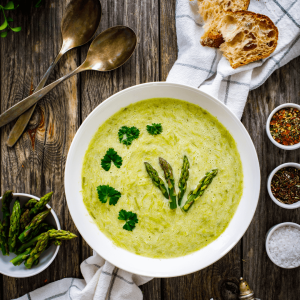 Creamy Asparagus Soup - in a bowl on a table with A side of bread and some seasonings. 