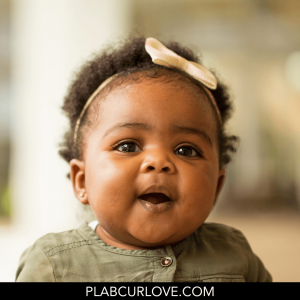 Baby girl with curly hair, wearing a headband.